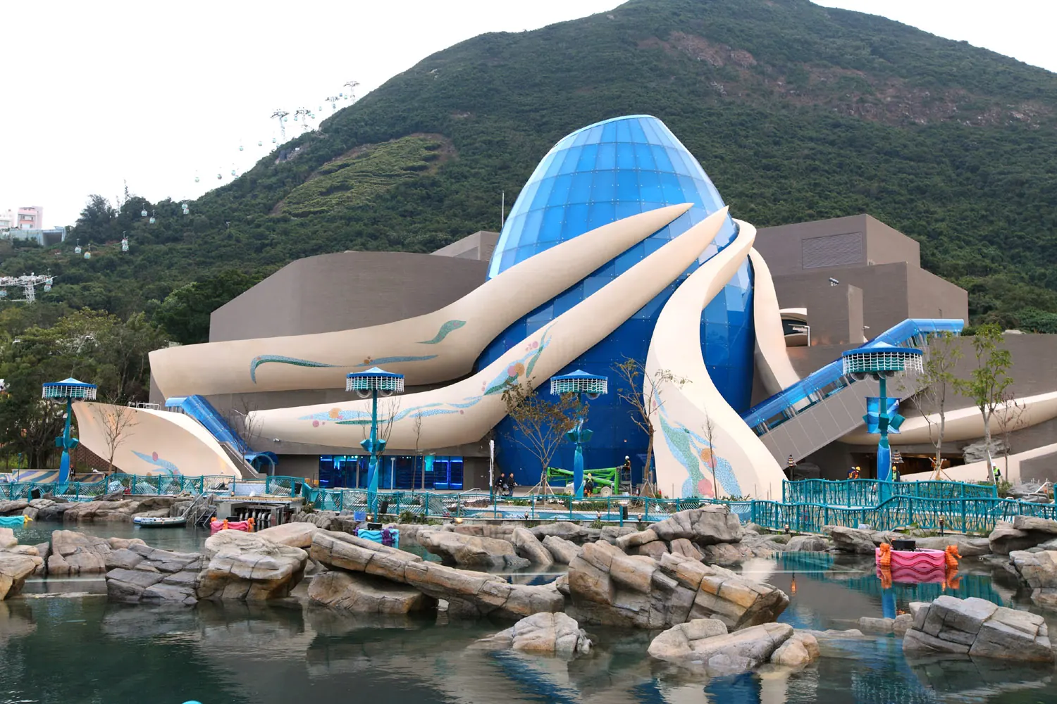 A blue glass dome with sweeping white fins behind a rocky pool at Ocean Park